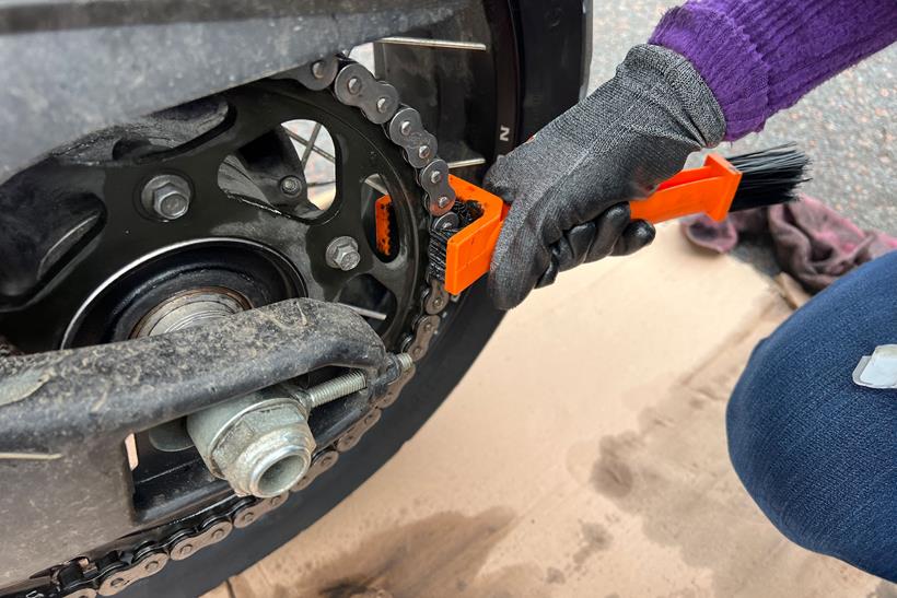 Motorcycle chain being scrubbed with a chain brush