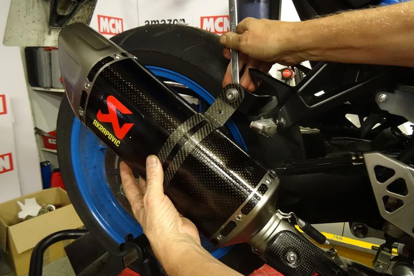 Akrapovic exhaust being fitted to rear hanger of a motorcycle