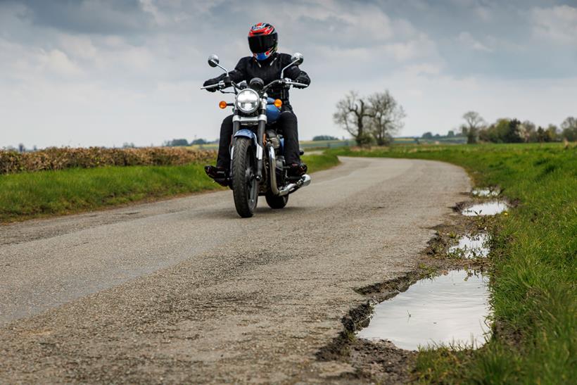 Motorcyclist riding alongside potholed road