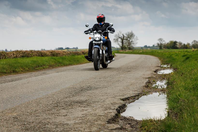 Motorcyclist rides alongside pothole littered road