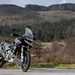2024 Triumph Tiger 1200 Rally Pro and Explorer bike leaning on side stand facing the camera with a forest and green hills background