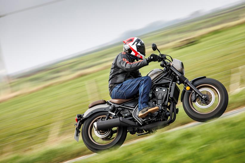 Honda CMX500 Rebel side shot of bike riding past with grassy field backdrop