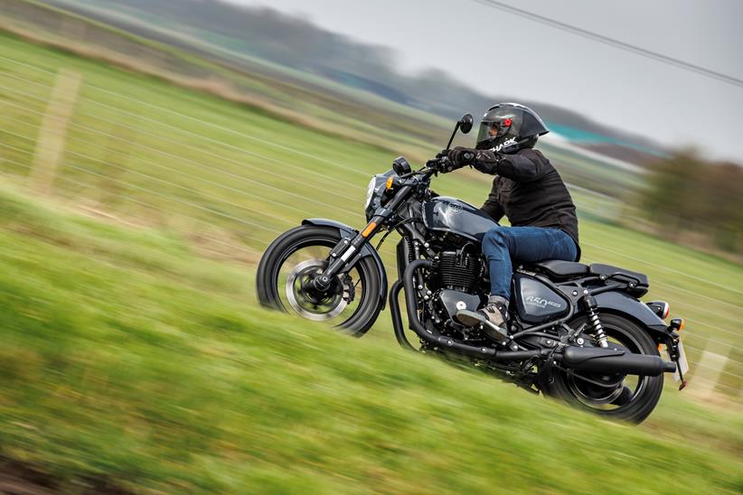 Royal Enfield Shotgun 650 riding past with a grassy backdrop