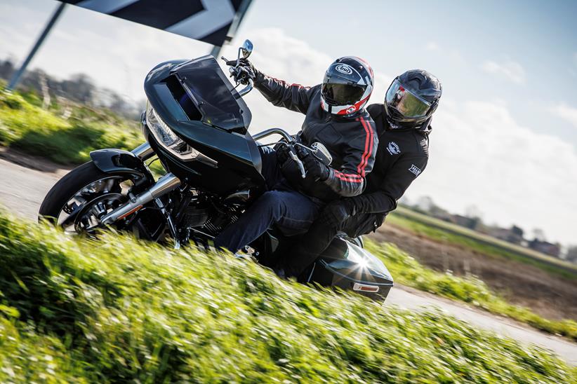 2024 Indian Challenger Dark Horse vs Harley-Davidson Road Glide - Harley riding past leaning into a corner with pillion