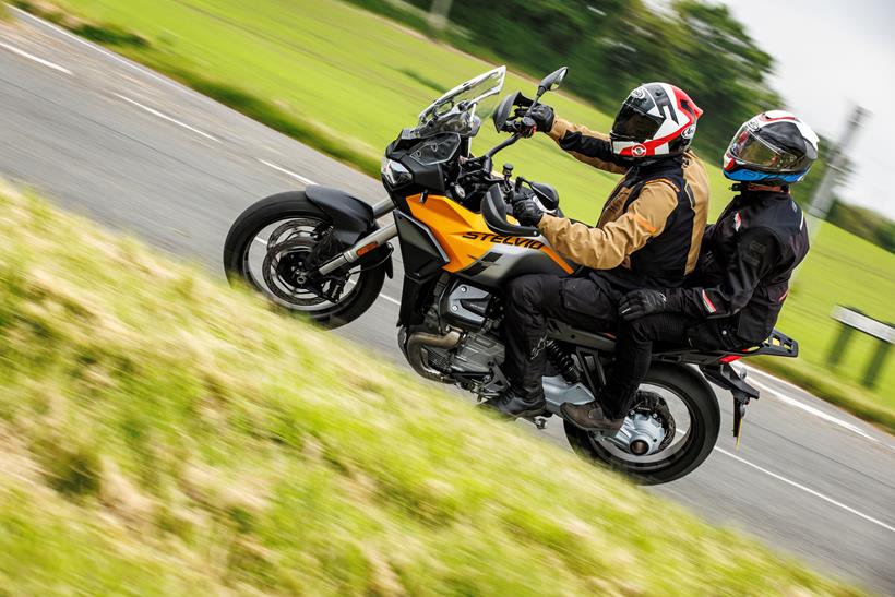 The 2024  Moto Guzzi Stelvio riding past the camera with a pillion on board