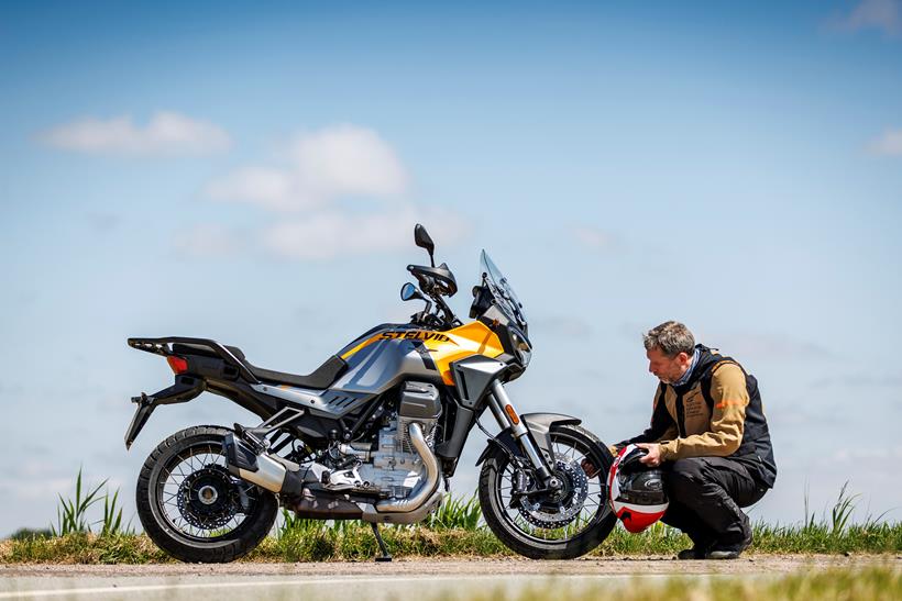 A static image of the 2024 Moto Guzzi Stelvio with the rider crouched by inspecting it