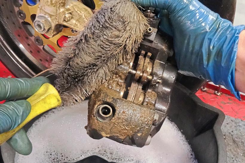 Cleaning a brake caliper with a brush over a bucket