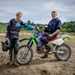 Two riders stand with Kawasaki off-road bike