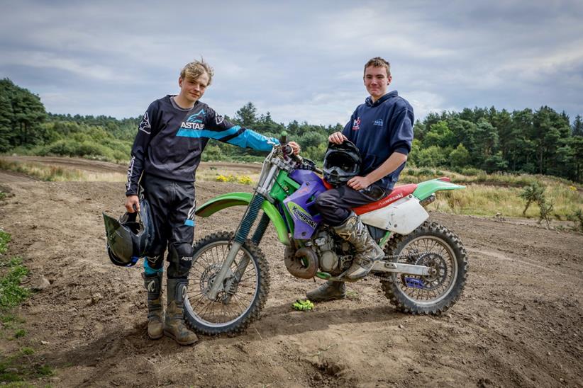 Two riders stand with Kawasaki off-road bike