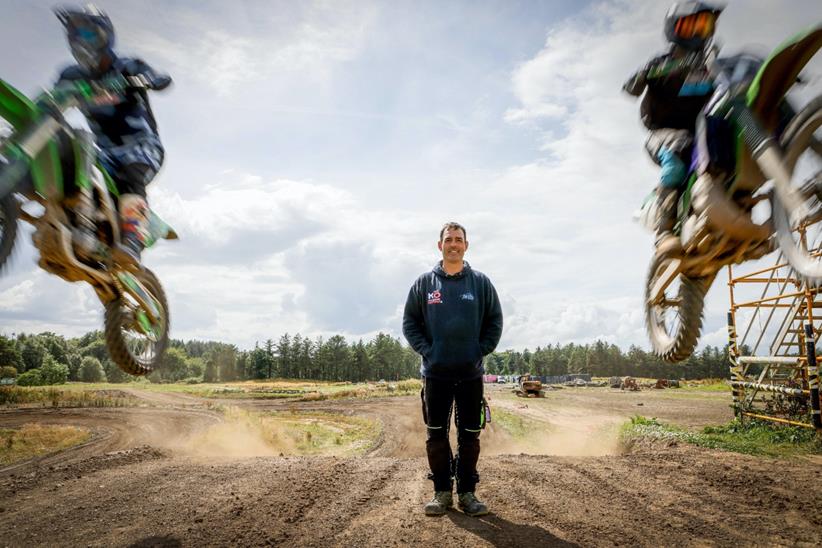 Club founder, David Paton, standing on motocross jump with two riders mid-air to either side of him