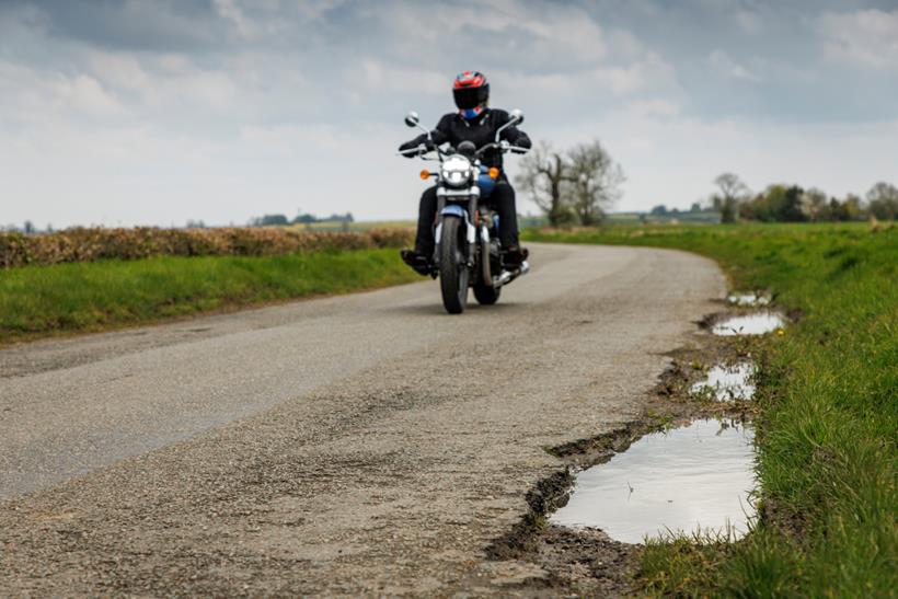 Motorcyclist on road with potholes to side