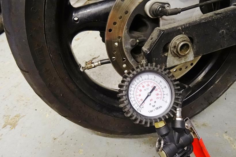 Checking a motorcycle tyre's pressure with a pressure gauge