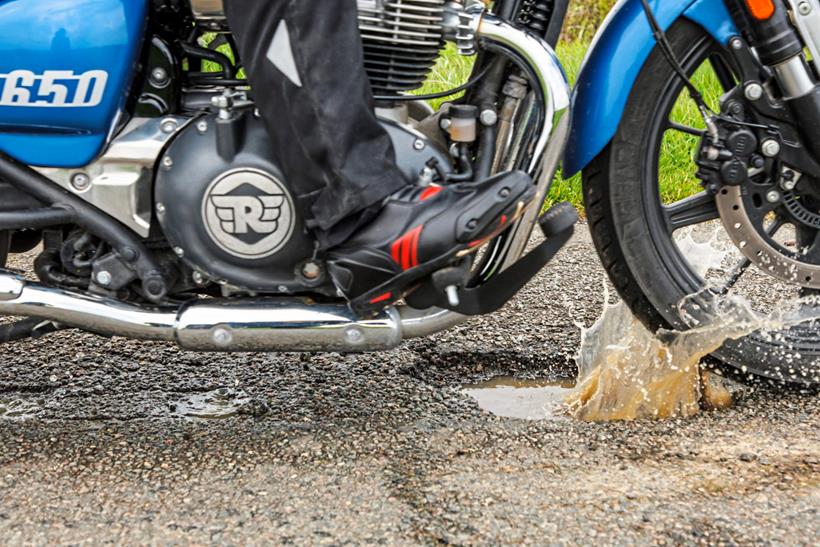 A motorcyclist drives through a pothole