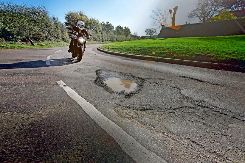 A motorcyclist is approaching a pothole on a corner