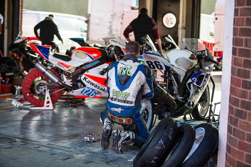 Riders work on their bikes in the garages