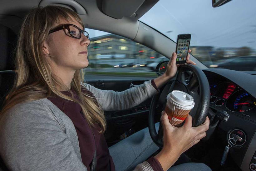 A driver using their phone and holding a coffee