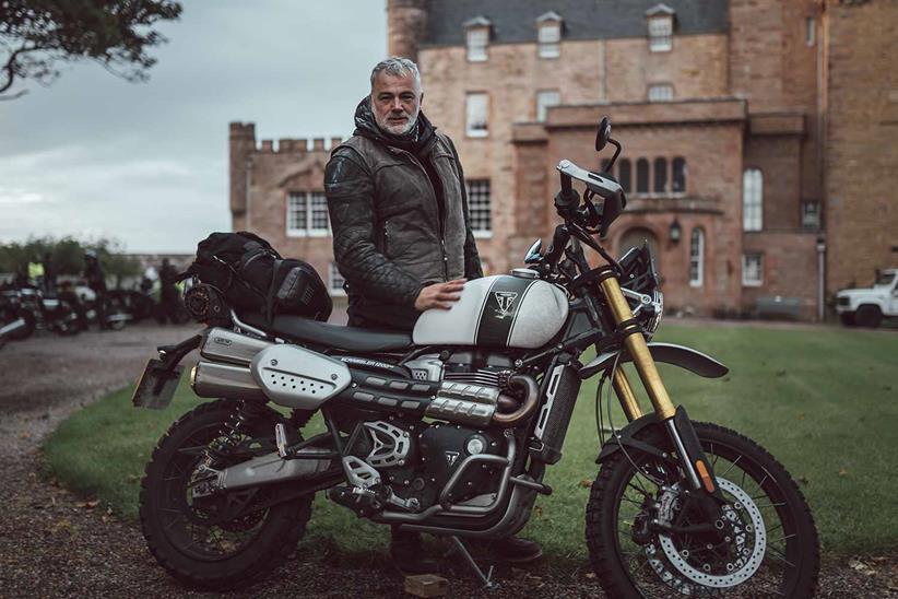 A rider stands with their Triumph Scrambler 1200